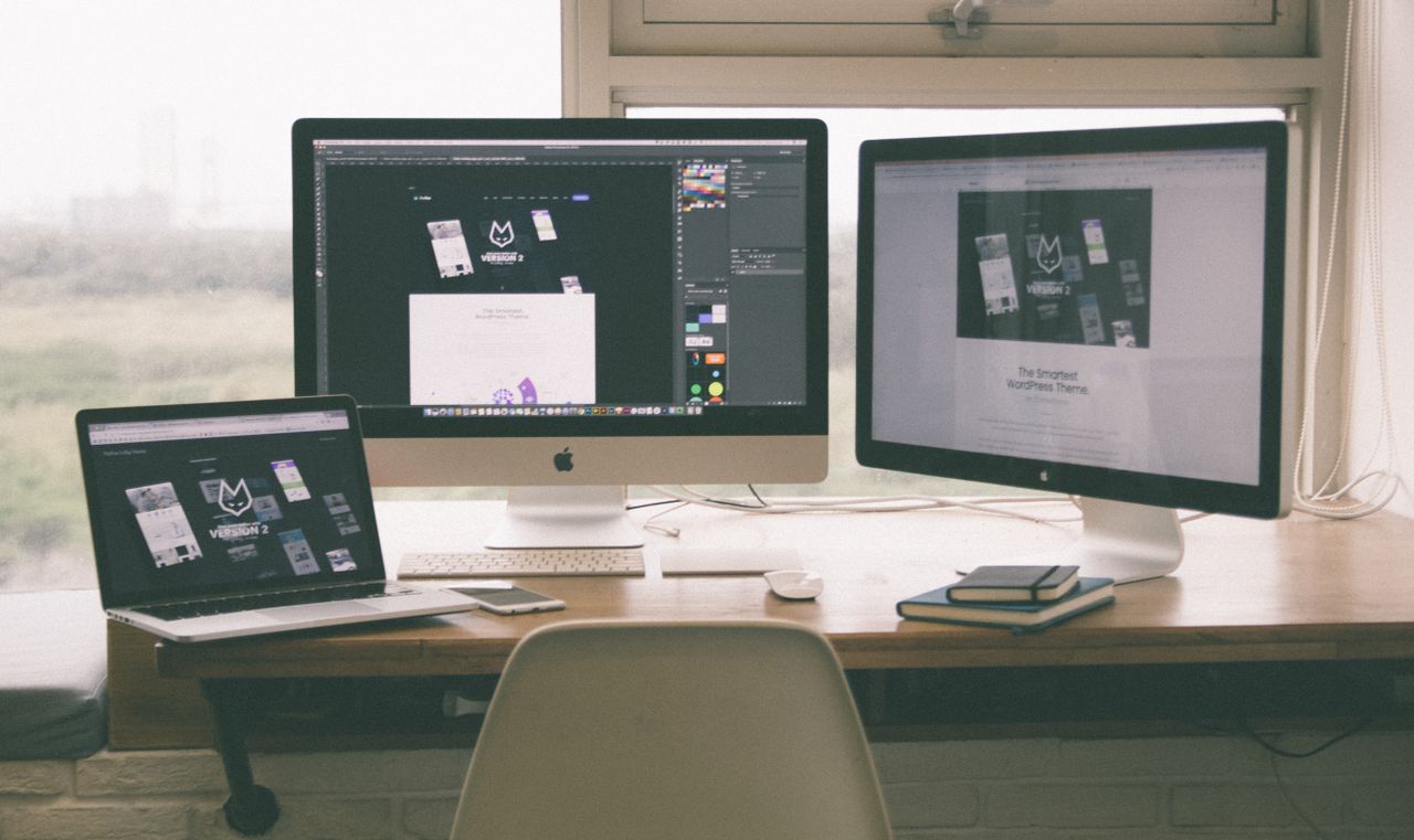 heros-img Stylish and efficient workspace with multiple monitors, laptop, and smartphone, showcasing a web design project.